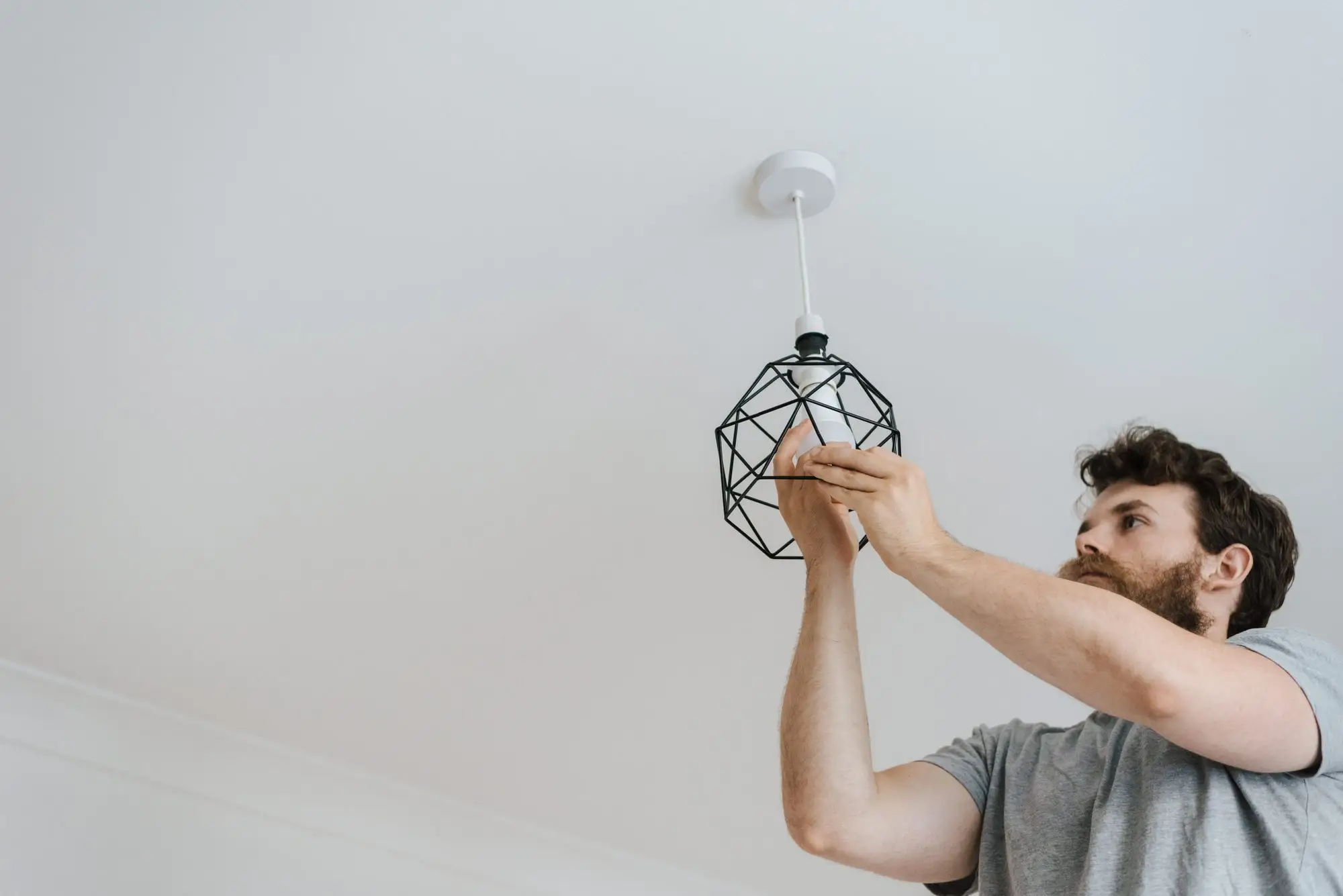 Homme fixant une suspension géométrique au plafond blanc