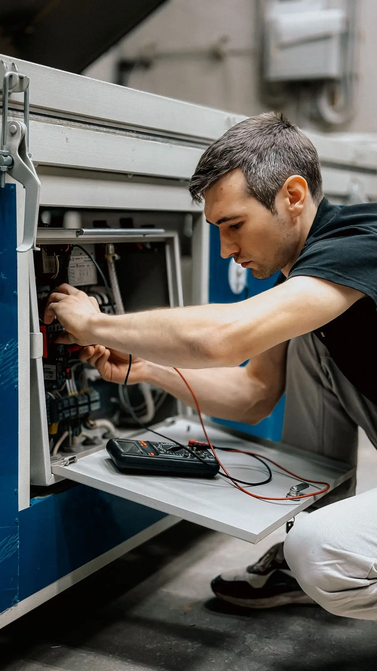 Technicien accroupi testant le câblage d’une armoire électrique