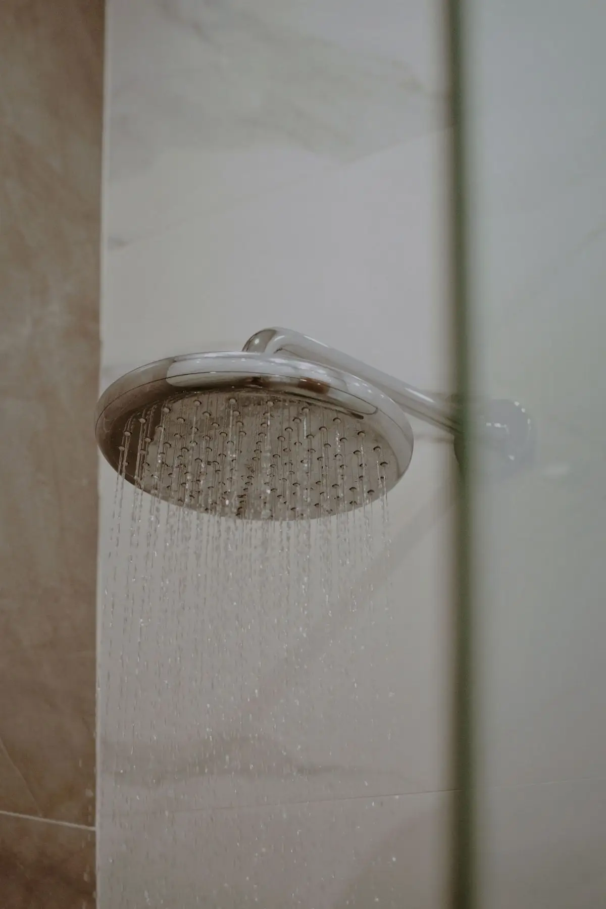 Pommeau de douche chromé, eau qui coule contre un mur clair