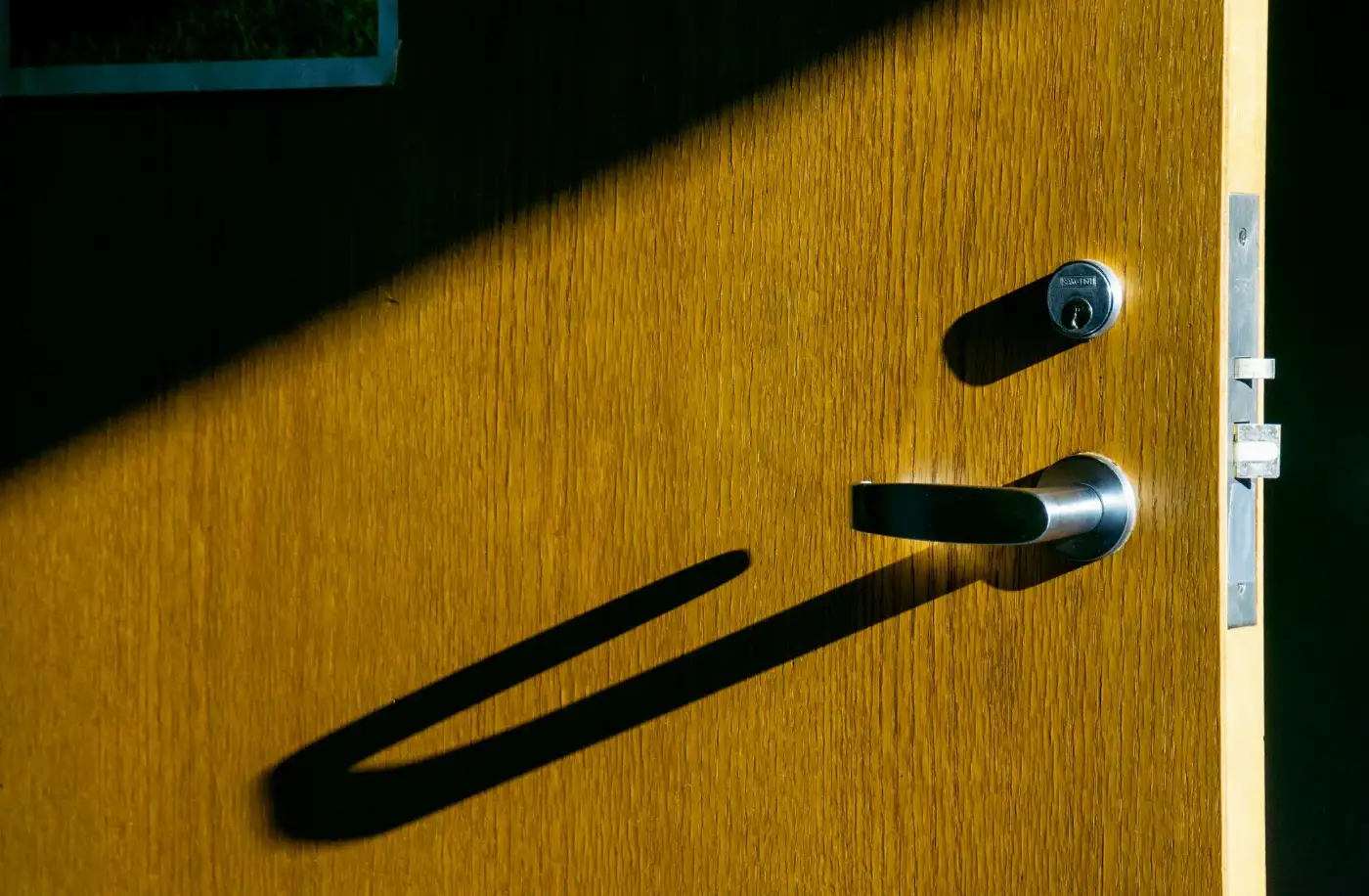 Poignée inox sur une porte en bois, ombre au soleil