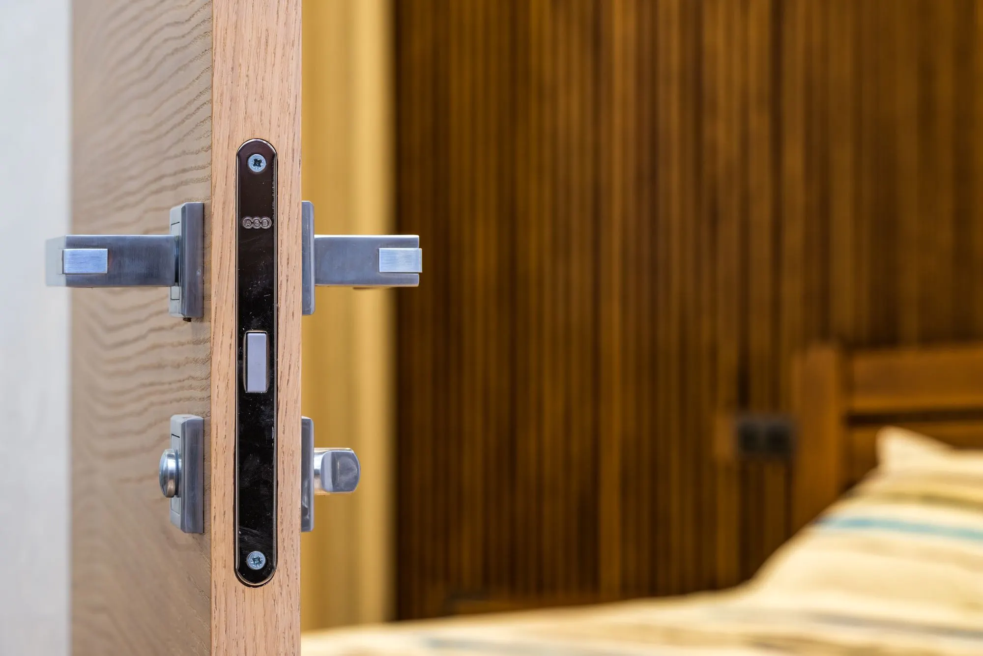 Porte en bois entrouverte, serrure encastrée et chambre au fond